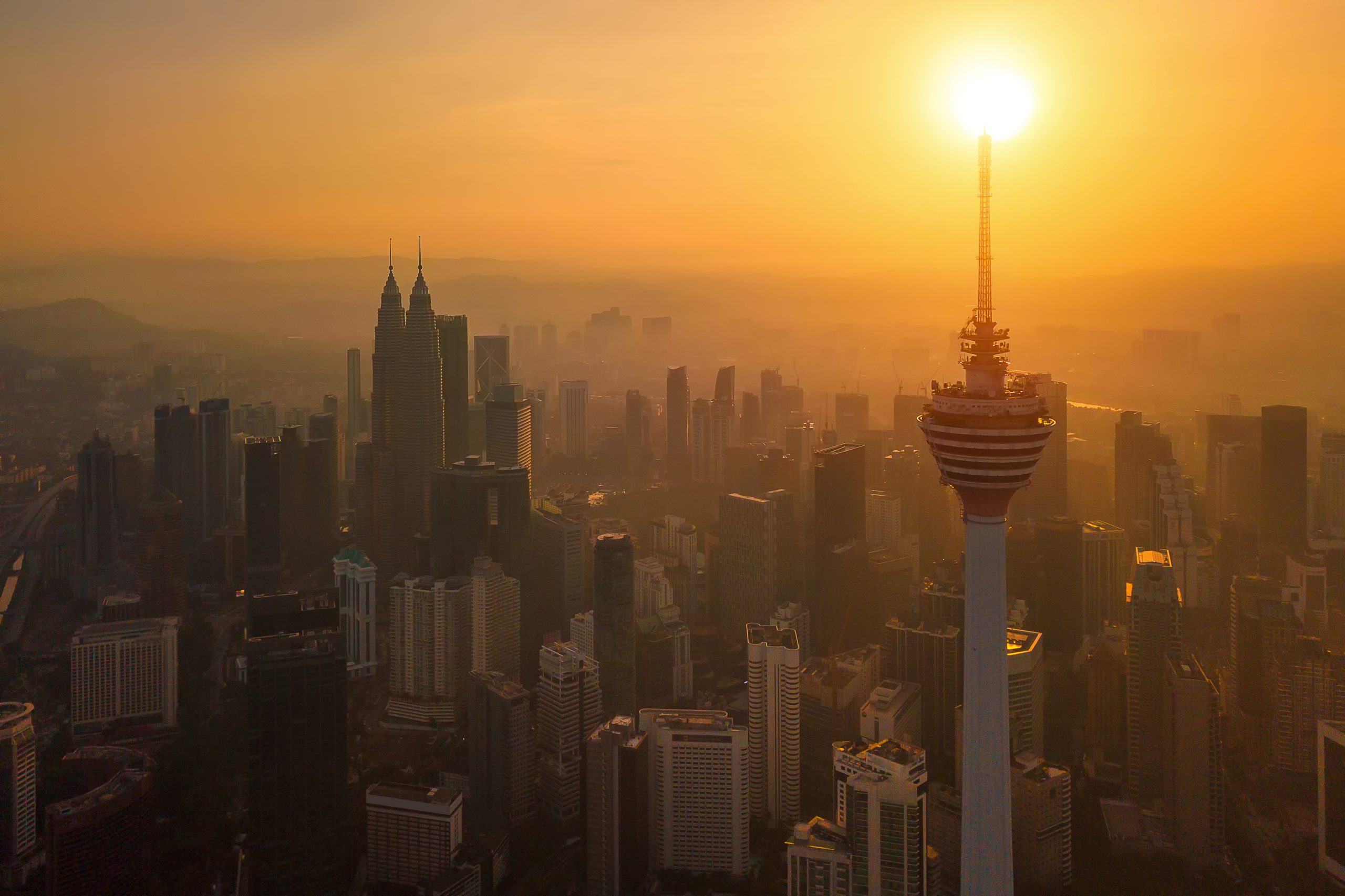 Menara Kuala Lumpur Tower with the sun. Aerial view of Kuala Lumpur Downtown, Malaysia. Financial district and business centers in urban city in Asia. Skyscraper and high-rise buildings at sunset.