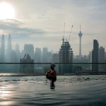 Woman enjoying cityscape of Kuala Lumpur from rooftop swimming pool. Urban scene with skyscrapers, Petronas Tower and Kuala Lumpur Tower, Malaysia