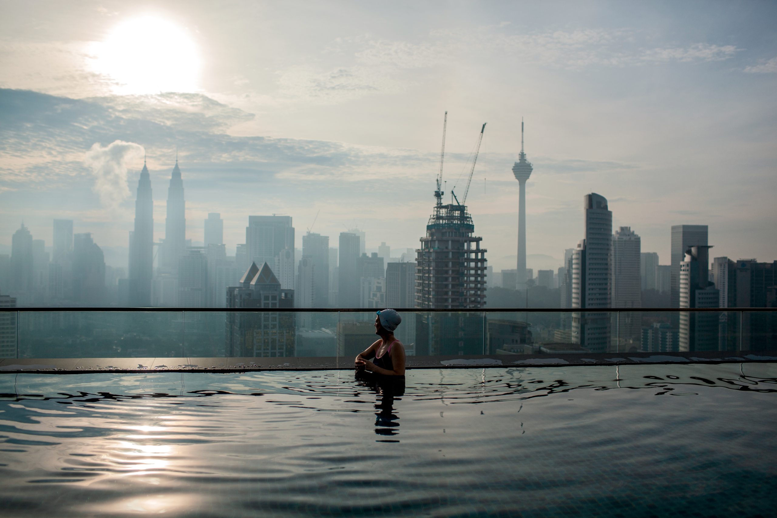 Woman enjoying cityscape of Kuala Lumpur from rooftop swimming pool. Urban scene with skyscrapers, Petronas Tower and Kuala Lumpur Tower, Malaysia